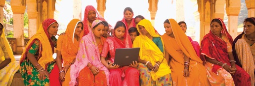 Group of twelve Indian women in colorful saris looking at a laptop computer